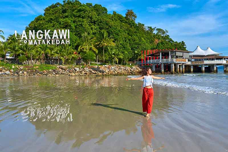 10 beautiful beaches in malaysia happy woman with outspread arms on the central beach in Langkawi tropical island.