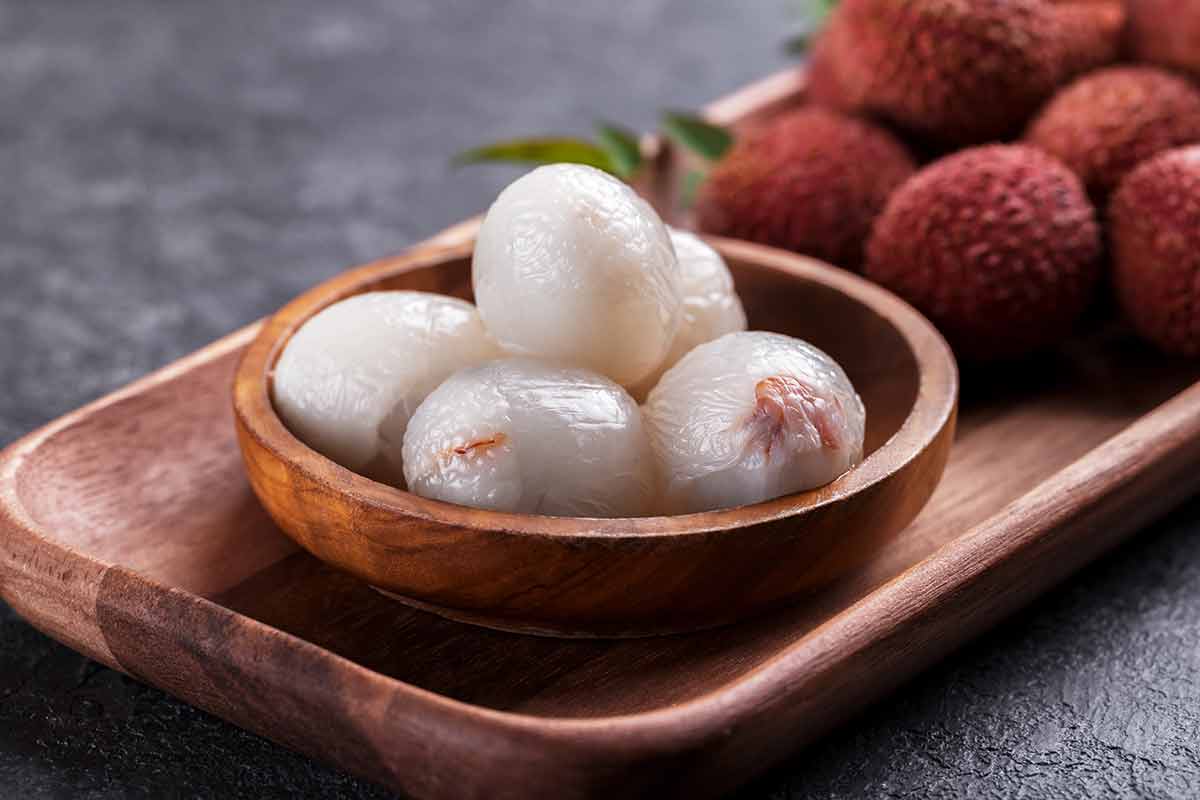 Ripe healthy peeled lychee fruit in a wooden bowl on black stone background