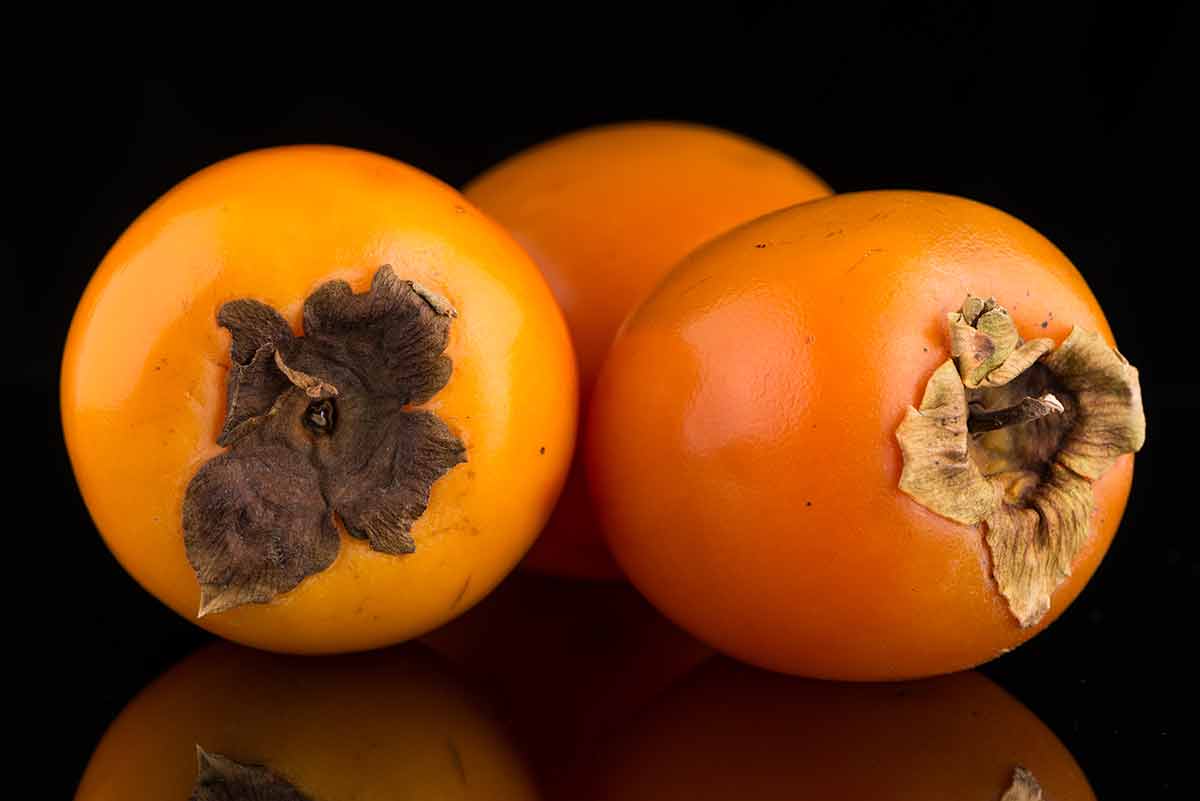 Three persimmons on a black table