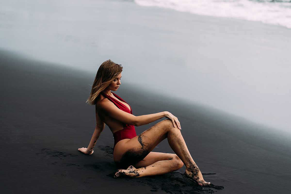 Woman in red swimsuit posing on a black sand beach