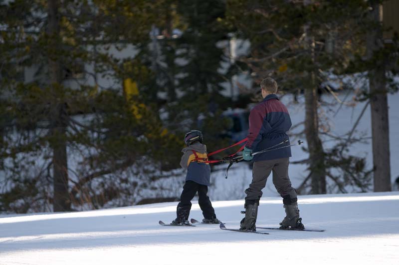 Dad teaching kid how to ski with a harness