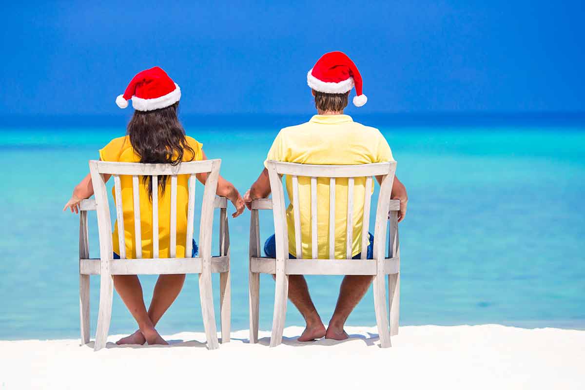 Christmas photos on the beach of couple sitting in chairs wearing santa hats