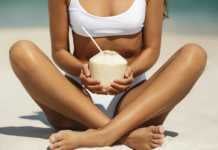 20 Things To Do In Malibu That Go Beyond Celebrity Spotting Malibu tanned woman in a white sports bikini sitting crossed-legged on the sand drinking juice from a coconut