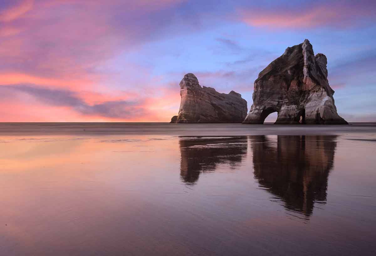 New Zealand Beaches Wharariki Beach elephant rocks reflected in glassy water with purple sky
