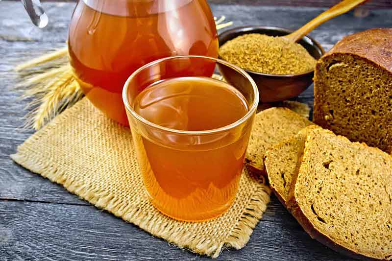 Polish drinks kvass glassful and glass jug on burlap, malt in a bowl, rye bread and ears on a wooden plank