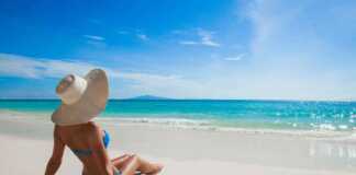 woman in blue bikini and floppy hat sitting on the sand in one of Spain beaches