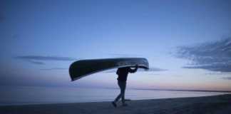 Warmest beaches in Canada man carrying a canoe at dusk on Wasaga Beach