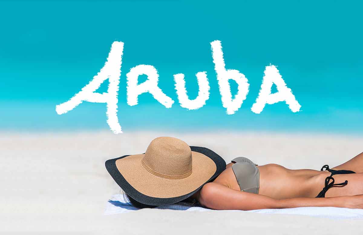 aruba beaches ARUBA title written on sky above beach travel bikini suntan woman sleeping relaxing covering face with hat doing siesta. ARUBA text in blue ocean copyspace above.