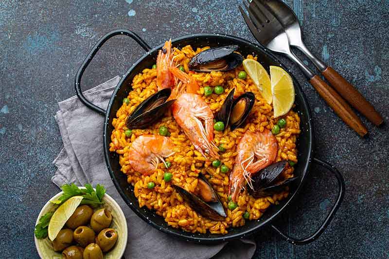 barcelona things to do at night Classic dish of Spain, seafood paella in traditional pan on rustic blue concrete background top view.