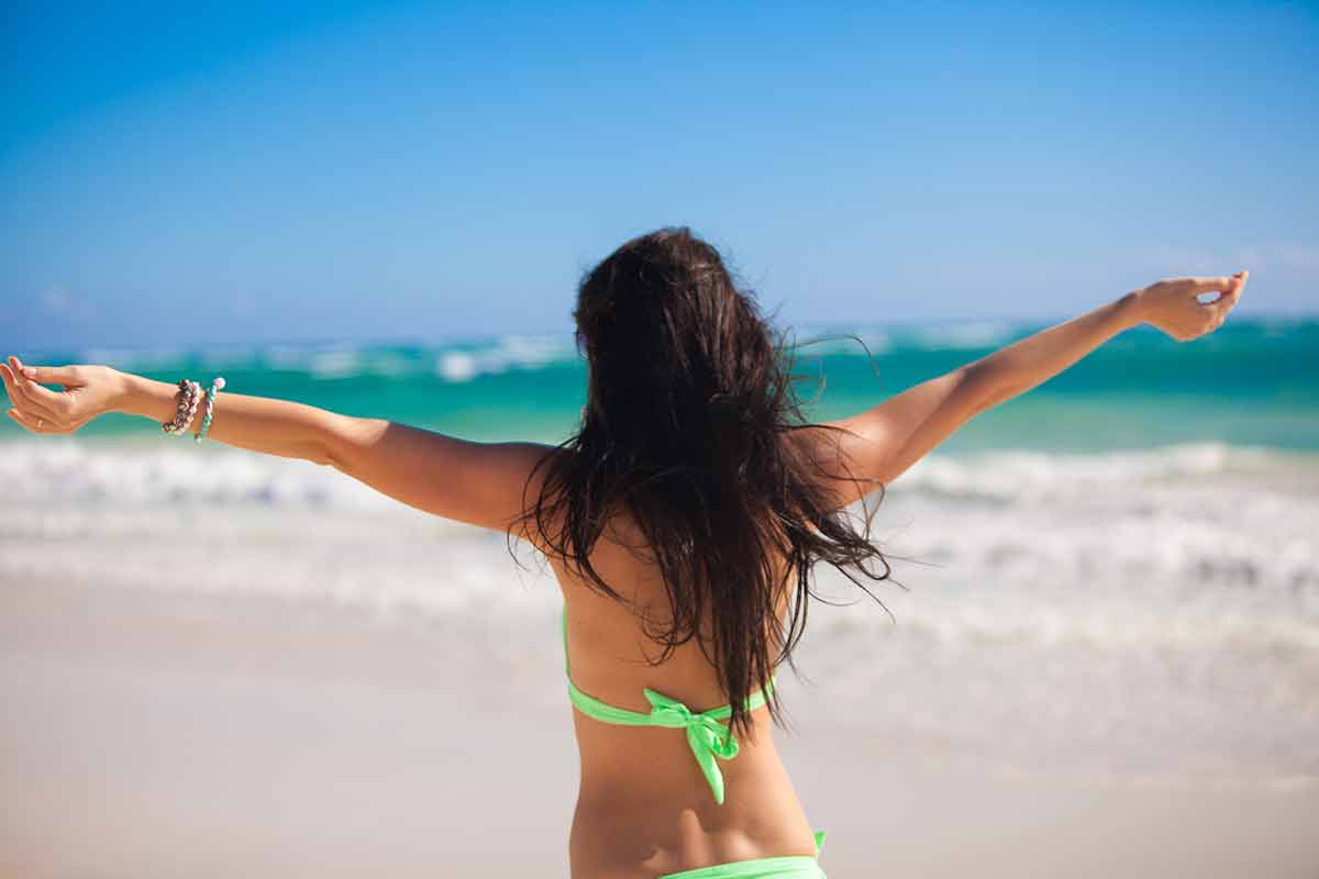 Woman enjoying the holiday spread her hands on a white, tropical beach