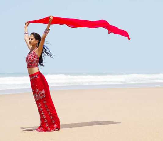 beaches India Indian woman in red sari holding a red scarf above her head on the beach