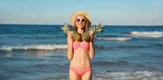woman holding two pineapples in front of the ocean