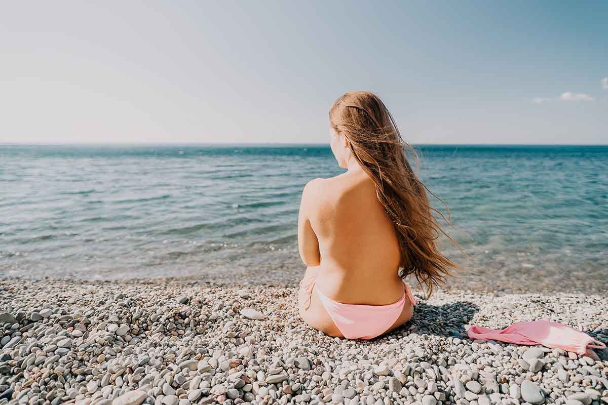 woman in pink bikini bottom sitting with her back to the camera on a beach