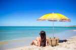 20 Stunning Beaches In Haiti long-haired woman sitting on a beach under a yellow umbrella