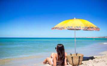 long-haired woman sitting on a beach under a yellow umbrella