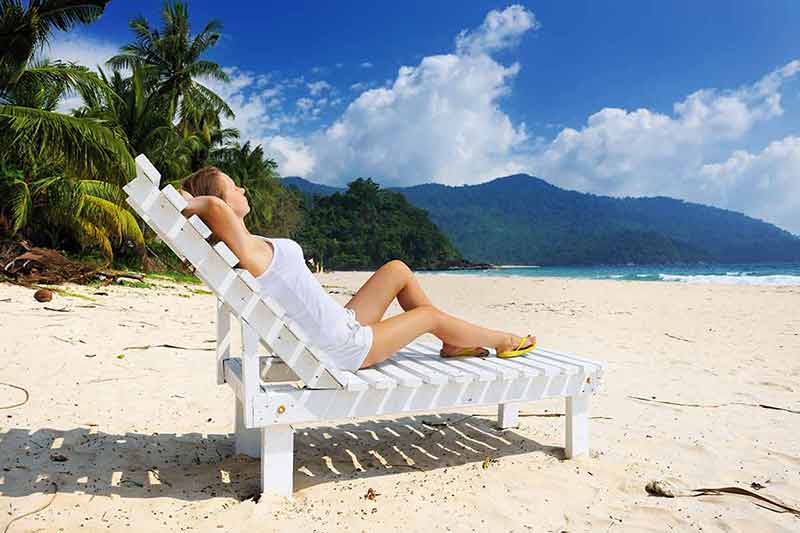 beaches in malaysia girl wearing white singlet and shorts sitting on a white sun lounge