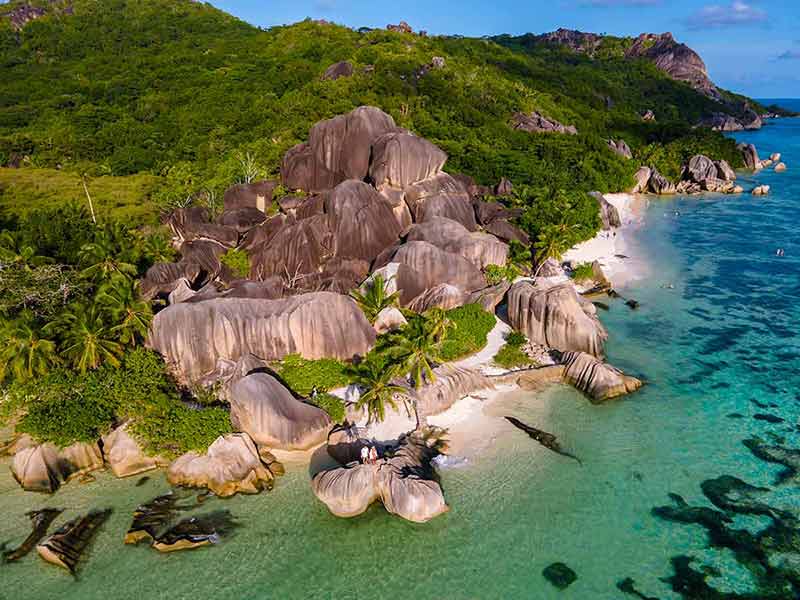 beaches in seychelles rocks and green hills with couple standing near the water