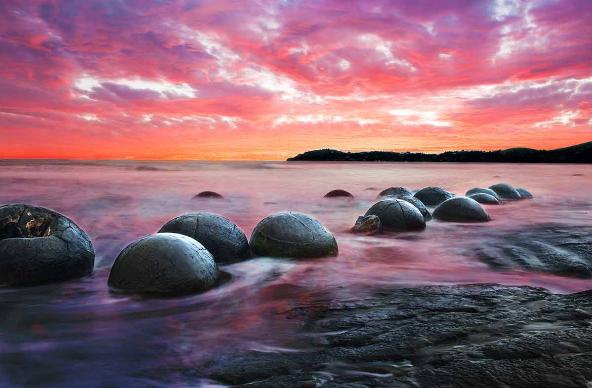 beaches new zealand sunset and long exposure of rocks in the ocean