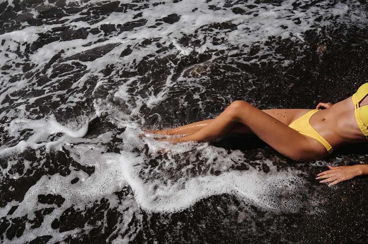 tanned female body in yellow bikini lying on the beach