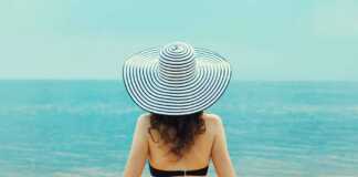 woman wearing a striped hat looking at the ocean photo taken from behind