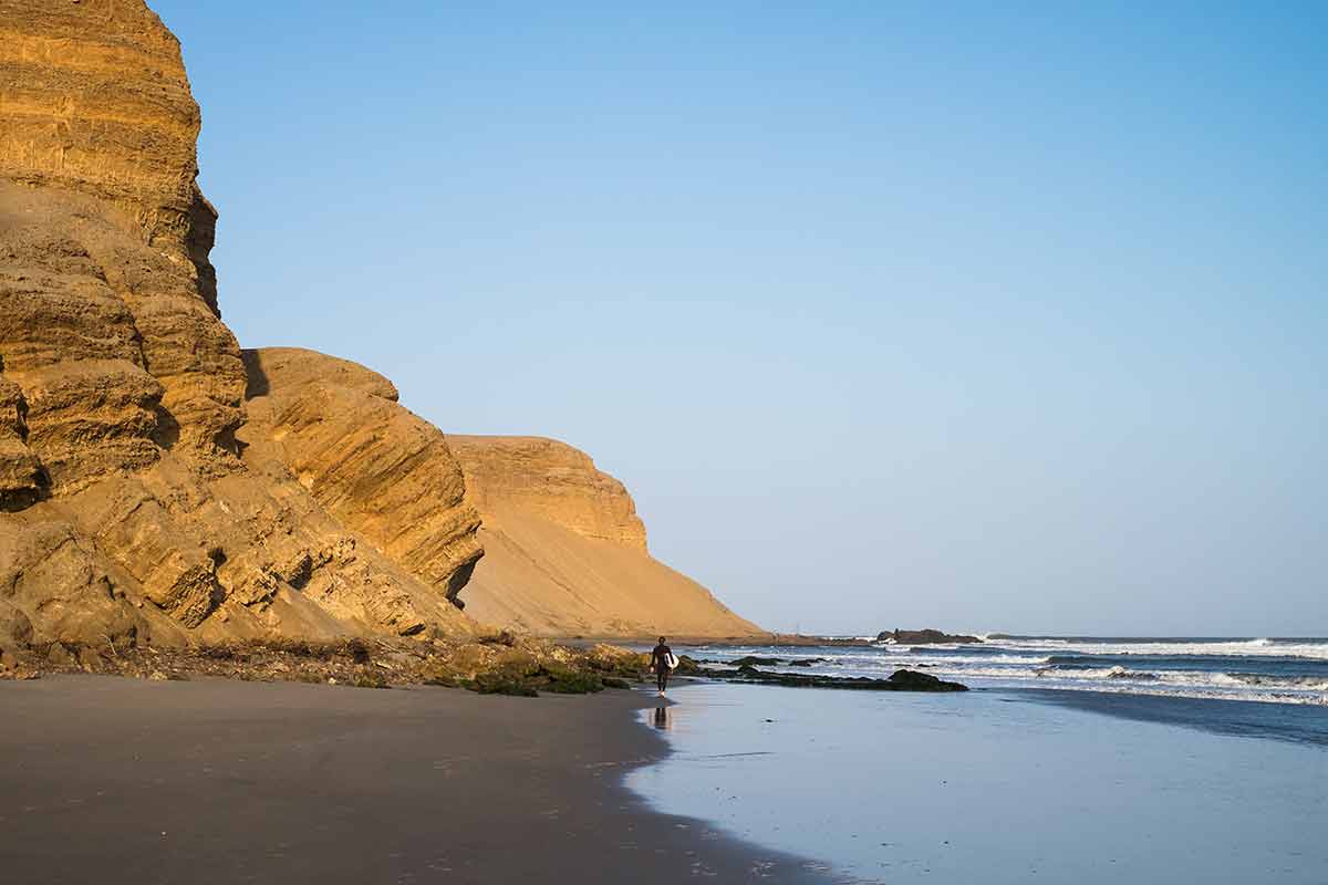 beautiful beaches in Peru Chichama Beach surfer and soaring rock cliff
