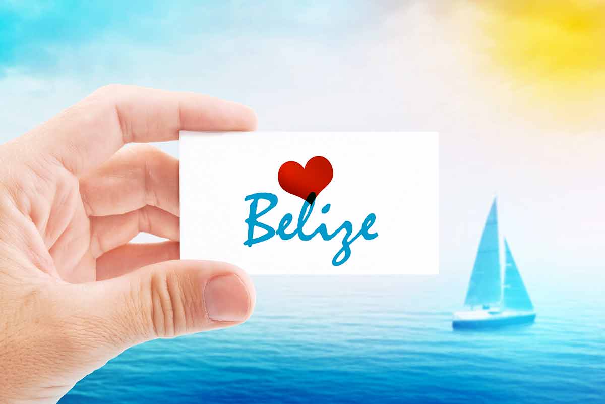 belize beaches Person Holding Visiting Card for Summertime Holiday Message Love Belize and Sailboat at Sea in Background.