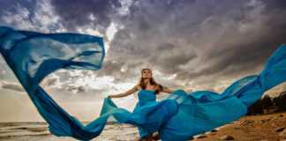best beaches in scotland redheaded woman wearing a flowing blue dress on a rocky sandy beach with dramatic clouds