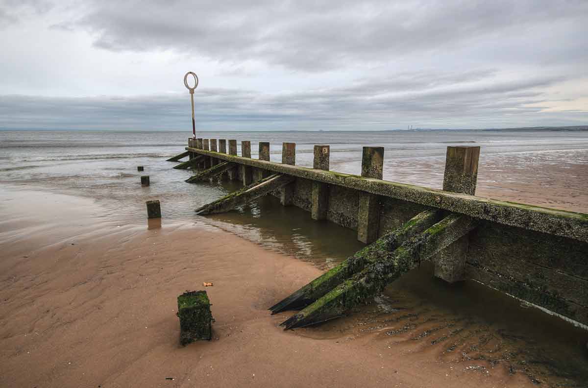 Old wood and stone groyne structure covered with green algae on Portobello beach in low tide with North sea in the backgroud on overcast day