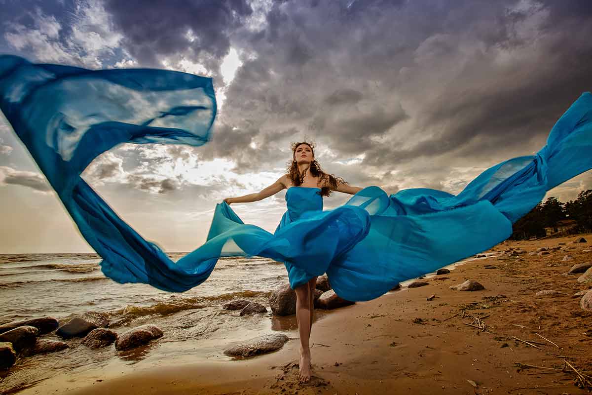 best beaches in scotland redheaded woman wearing a flowing blue dress on a rocky sandy beach with dramatic clouds