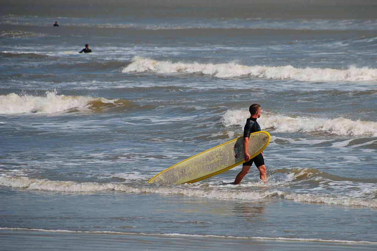 best beaches in texas for families a surfer dragging his surfboard on a Galveston beach