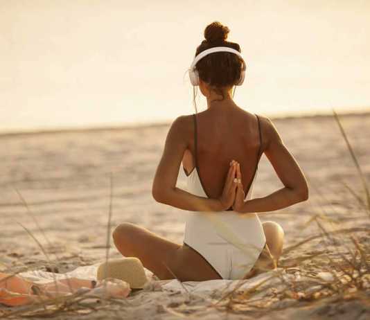 best beaches in uk sexy woman in white swimsuit wearing headphones doing yoga on the beach
