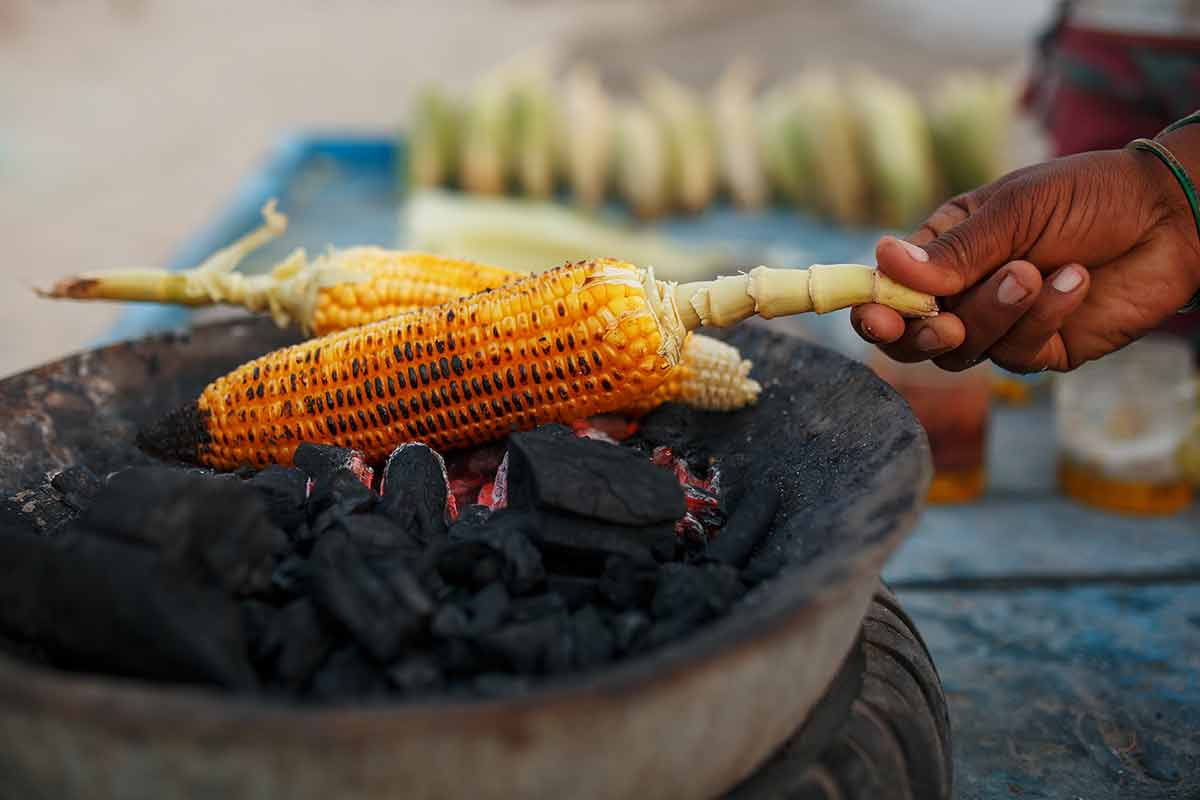 best indian street food Close-up hands of female street vendor is rubbing a roasted sweet corn cob with lemon and spices
