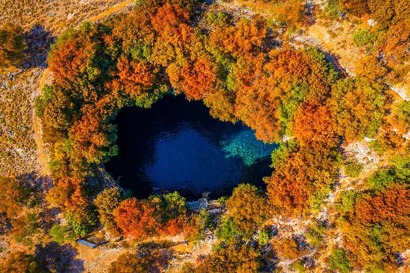 best time of the year to visit greece aerial view of Melissani lake with autumn foliage around it