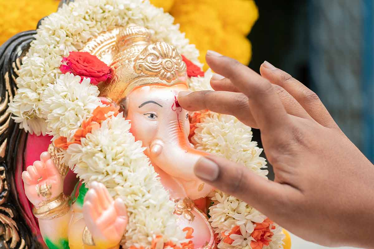 best time of year to visit india hands applying Tilak or Kumkum to Lord Ganesha