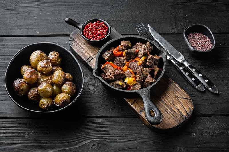 best time to visit ireland uk Beef meat and vegetables stew served, in cast iron frying pan, on black wooden background