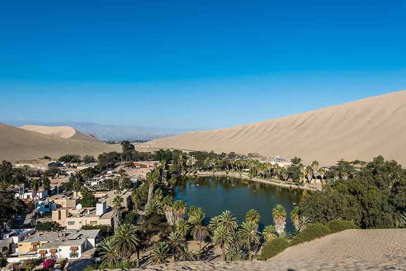 best time to visit peru lagoon surrounded by sand dunes and the town
