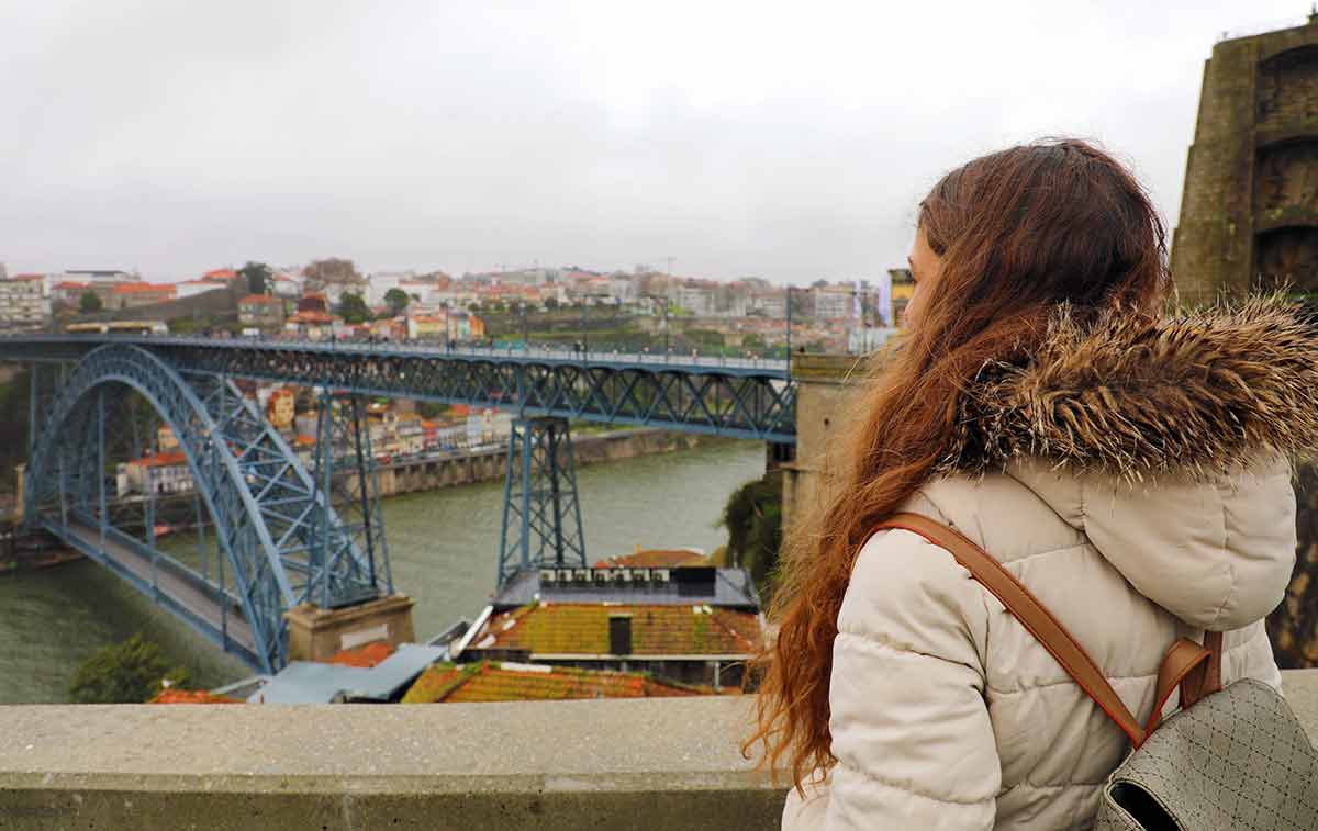 best time to visit porto portugal rear view of young backpacker woman enjoying Porto sight in winter time