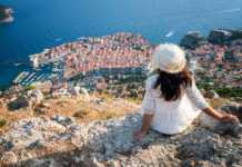 best time visit Croatia woman in white dress and white hat looking down at Dubrovnik view