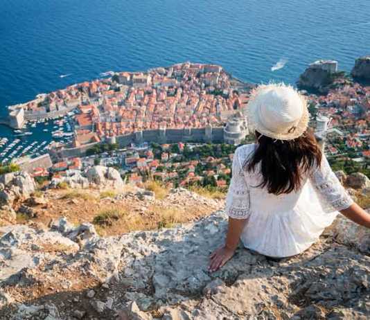 best time visit Croatia woman in white dress and white hat looking down at Dubrovnik view