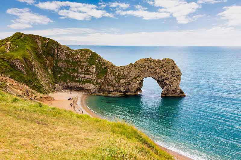 best uk beaches Durdle Door, travel attraction on South England, Dorset in sunny summer day with calm azure sea and blue sky. View from top of cliffs.