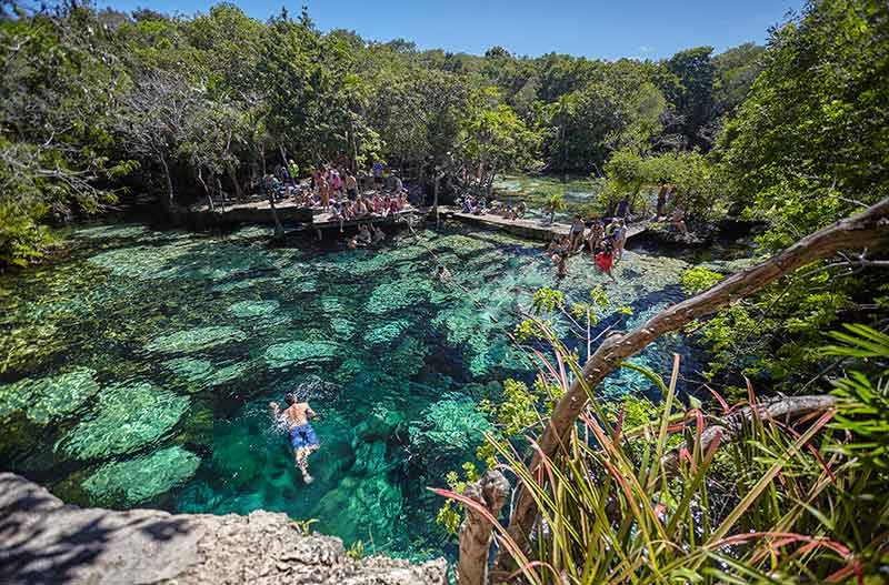 cenote azul in mexico man swimming in clear water with crowds of people on the pontoon
