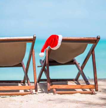 Santa Claus hats on beach loungers with turquoise sea water and white sand.