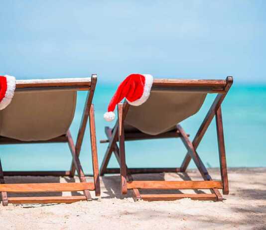 Santa Claus hats on beach loungers with turquoise sea water and white sand.