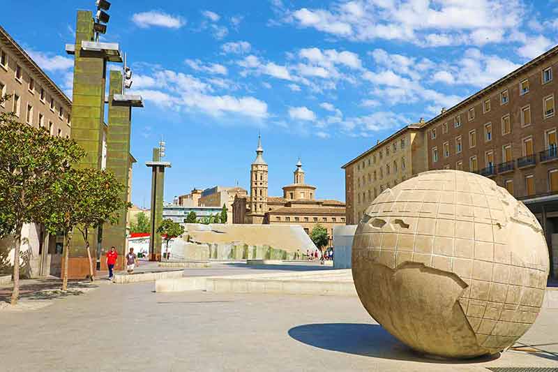 cities in spain list globe sculpture in the square with historic buildings in the distance