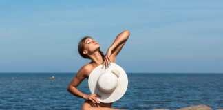 nude woman sitting on a rock covering up with a hat