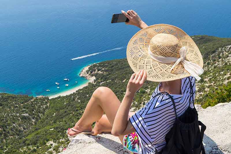 croatia no beaches woman wearing straw hat sitting at the edge of a cliff taking a selfie