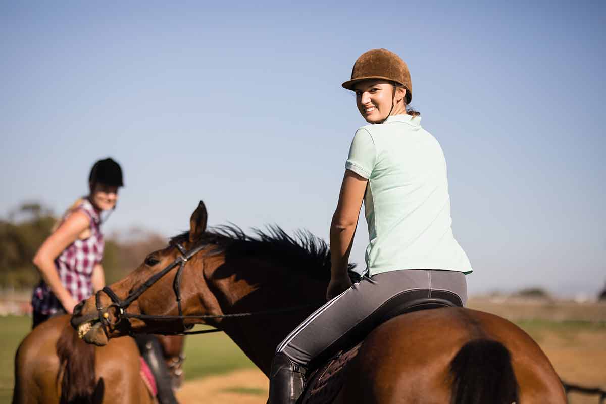 day trips from houston for couples female friends looking over shoulder while sitting on horse during sunny day.