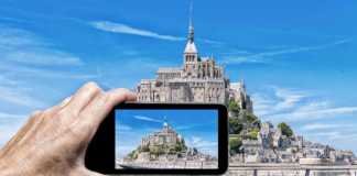 day trips from paris to mont st michel Female hand with smartphone taking a picture of Mont Saint Michel