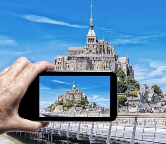 day trips from paris to mont st michel Female hand with smartphone taking a picture of Mont Saint Michel