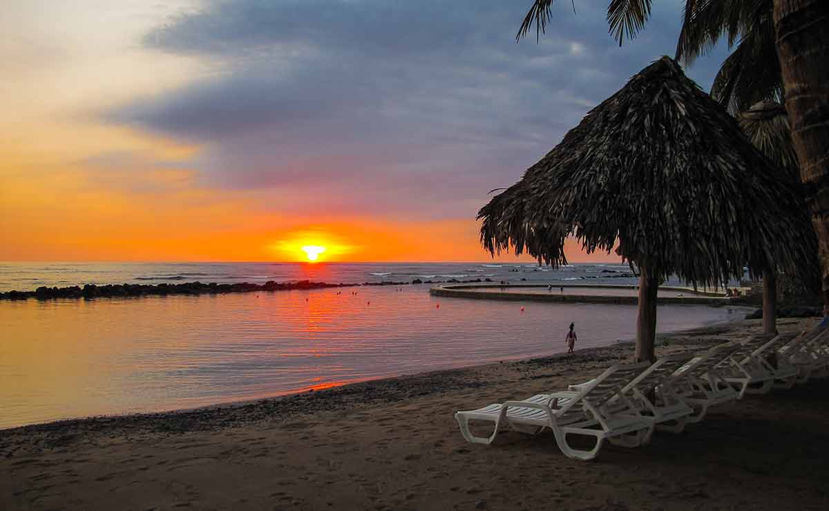 el salvador pacific beach thatched umbrellas and white deck chairs on the beach at sunset